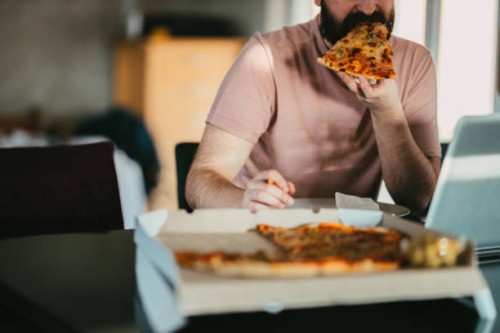man working from home eating take-out pizza and using a laptop - junk food stock pictures, royalty-free photos & images