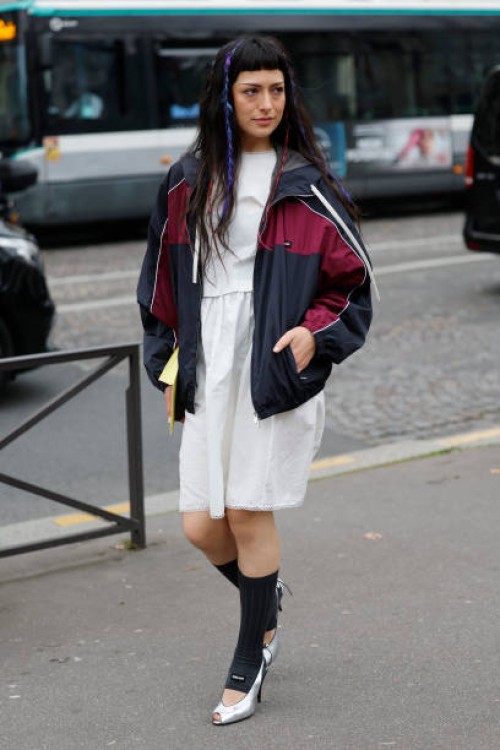 Maria Bottle wears white midi dress, blue and red Miu Miu jacket, grey Miu Miu socks, silver heels, outside Miu Miu, during the Womenswear...