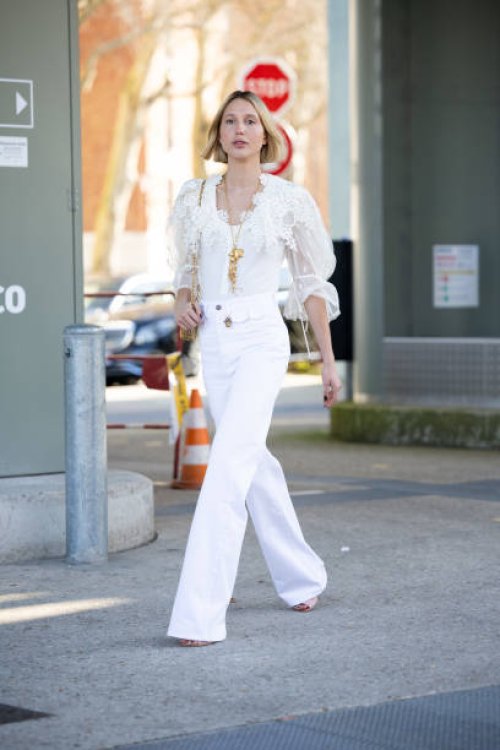 Maria Olympia of Greece and Denmark wears a gold necklace, a white lace puffy sleeves shirt, beige heels, white high waist flared trousers and a gold...