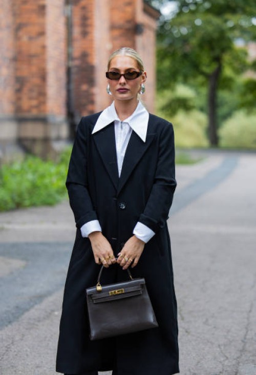 Maria Wos wears black coat, white blouse, Hermes bag, Holzweiler sunglasses, silver earrings at Oslo Fashion Week 2024 on August 27, 2024 in Oslo,...