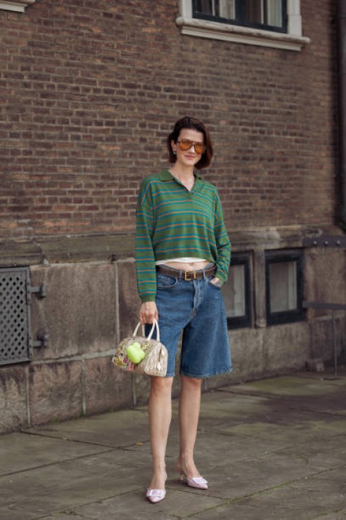 Marianne Theodorsen wears blue denim shorts, pink pointy shoes, green long sleeve shirt and orange sunglasses outside the Mark Kenly Domino Tan show...