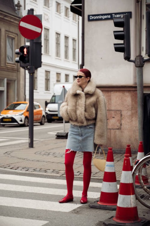 Marianne Theodorsen wears red tights, red shoes, a denim mini skirt, a brown fur coat, and a pale yellow bag outside The Garment during the...