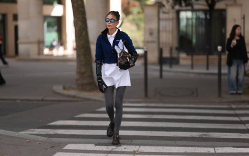 Masha Lobanova is seen wearing several small gold hoop earrings, sporty black sunglasses with blue mirrored lenses and a gold Miu Miu logo at the...