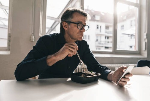 mature businessman checking cell phone during lunch break in office - junk food stock pictures, royalty-free photos & images