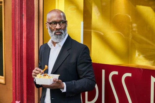 mature businessman eating french fries in front of snack bar - junk food stockfoto's en -beelden