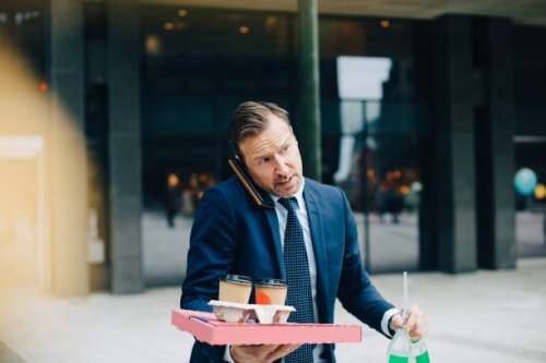 mature businessman talking on mobile phone while carrying food and drinks in city - junk food stock pictures, royalty-free photos & images