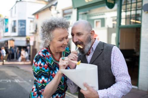 mature couple sharing a bag of chips outdoors - junk food stock pictures, royalty-free photos & images