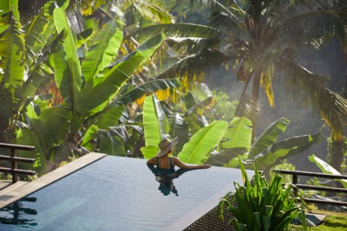 mature fit asian woman relaxing on edge of infinity pool, admiring jungle view with early morning mist - travel stock pictures, royalty-free photos & images