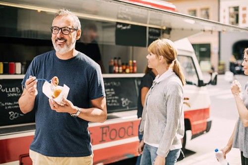 mature man eating food while standing against truck at street - junk food stock pictures, royalty-free photos & images