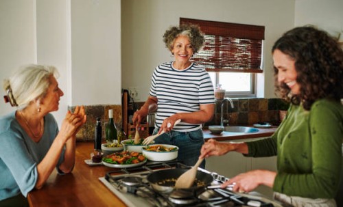 mature women laughing while cooking together in the kitchen of their vacation rental - food stock pictures, royalty-free photos & images