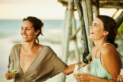 medium shot of woman laughing with friends on beach at tropical resort at sunset - fashion stock pictures, royalty-free photos & images