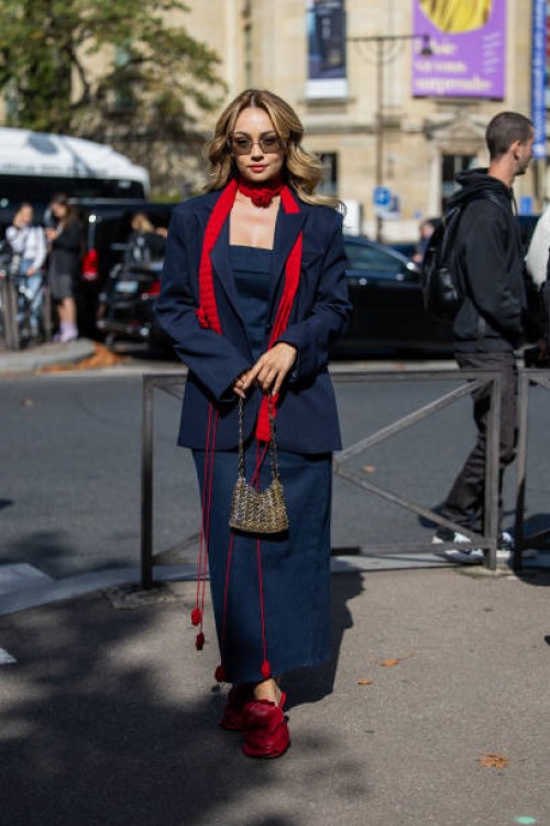 Merve Görgöz wears navy blazer, dress, red scarf, Miu Miu sunglasses, sequined Paco Rabanne bag, heels outside Miu Miu during the Womenswear...