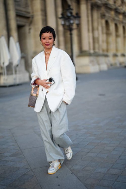 Mia Kong wears gold hoop earrings, gold layered necklaces, white oversized blazer jacket, light green blue loose pants, light gray monogram Side...