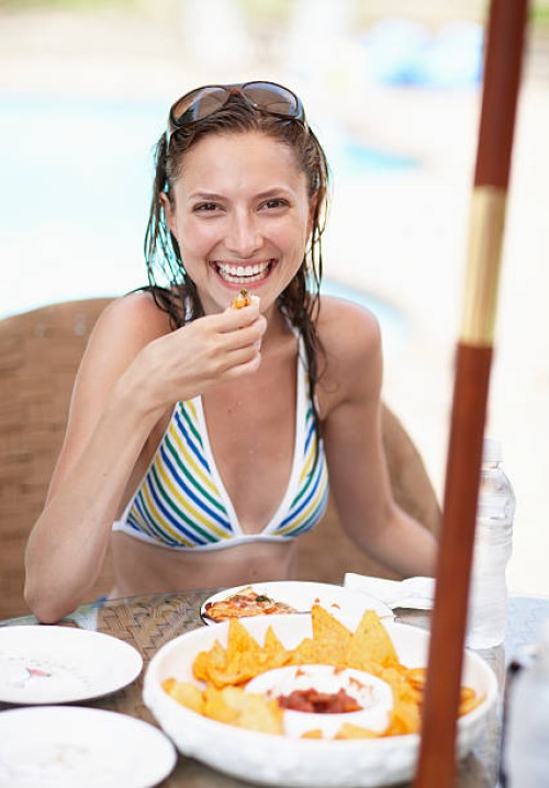 mid-adult woman in bikini eating nachos - junk food stock pictures, royalty-free photos & images
