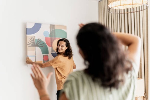 mid adult man asking his wife for help to put the frame on the wall in living room at new house - home decoration stock pictures, royalty-free photos & images