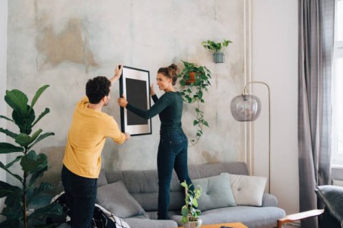 mid adult man passing picture frame to girlfriend against wall at new home - home decoration stock pictures, royalty-free photos & images