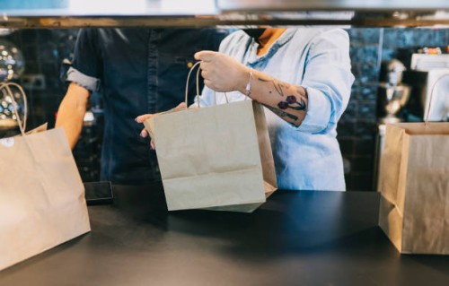 midsection of chefs working together while holding paper bags at restaurant kitchen counter - junk food stock pictures, royalty-free photos & images