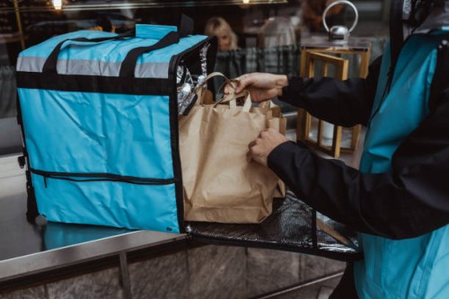 midsection of delivery man putting package order in backpack outside deli store - junk food stock pictures, royalty-free photos & images