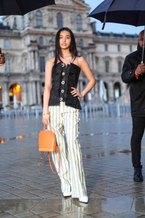 Mitsuki Kimura wears a black off-shoulder corset / top, a striped pants , an orange / brown leather bag, pointed shoes, outside Louis Vuitton, during...