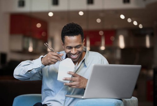 mixed race businessman using laptop and eating chinese food in living room - junk food stock pictures, royalty-free photos & images