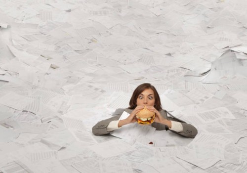 mixed race businesswoman drowning in paperwork eating hamburger - junk food stockfoto's en -beelden