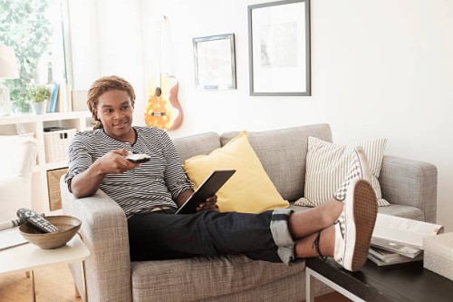 mixed race man watching television on sofa - home decoration stock pictures, royalty-free photos & images