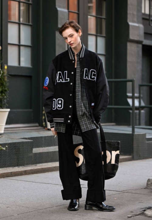 Model Aine O'Leary is seen wearing a varsity jacket, plaid shirt, black pants, black boots and black and white bag outside the Ashlyn show during...