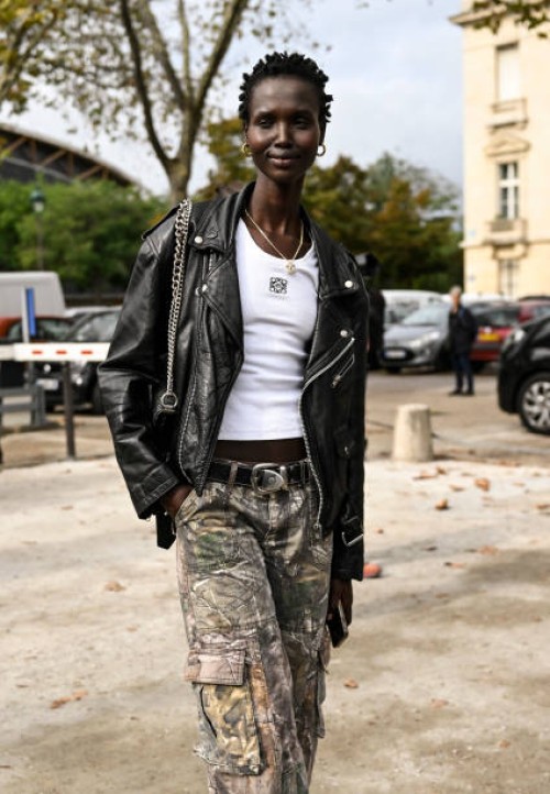 Model is seen wearing a black biker jacket, white Loewe shirt, cargo pants and black and silver chain bag outside the Chanel show during the...