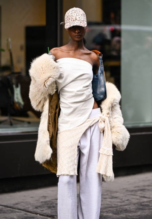 Model is seen wearing a cream fur coat, cream top and white pants, blue and tan bag, gold cuff and animal print hat outside the Lapointe show during...
