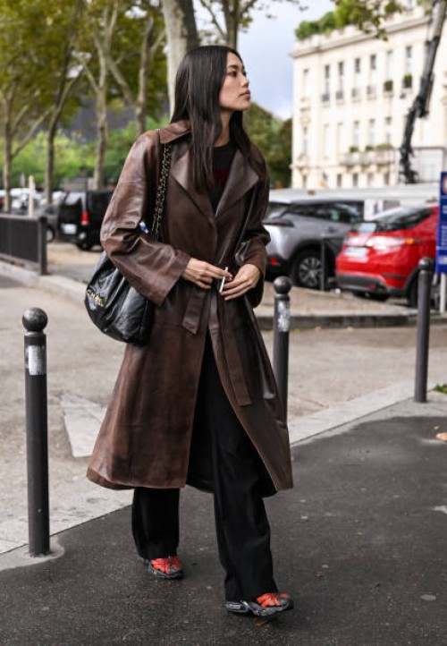 Model Jade Nguyen is seen wearing a brown leather trench coat and black and gold chain bag outside the Chanel show during the Womenswear...
