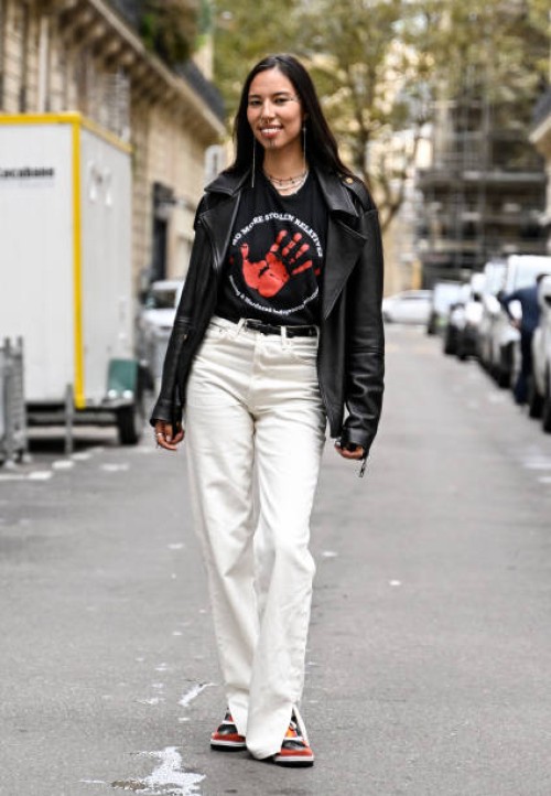 Model Quannah Chasinghorse is seen wearing a black leather jacket, a shirt that reads "No More Stolen Relatives", white pants and black belt outside...
