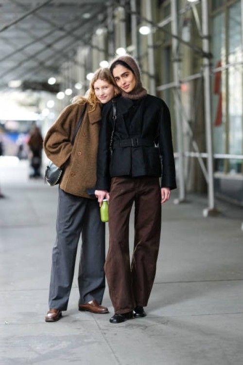 Model wears a brown oversized jacket, a turtleneck, gray pants, brown loafers ; a model wears a brown balaclava / hood, a black belted jacket, brown...