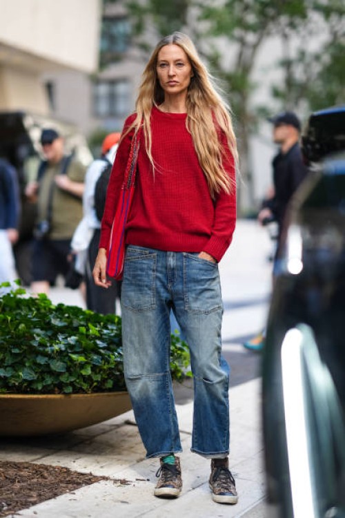 Model wears a red pullover , blue denim pants / jeans , outside Toteme, during New York Fashion Week, on September 10, 2024 in New York City.