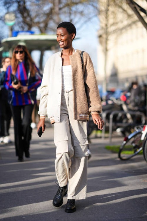 Model wears a white and brown wool jacket, a white low neck top, white pants, black leather shoes, outside Sacai, during the Womenswear Fall/Winter...