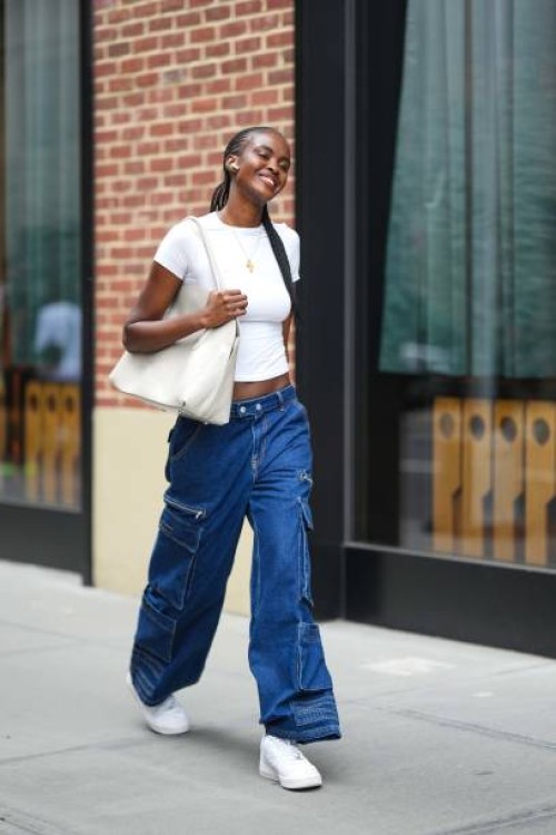 Model wears a white cropped t-shirt, blue cargo jeans pants, white sneakers shoes, a white bag, outside Tibi , during New York Fashion Week, on...