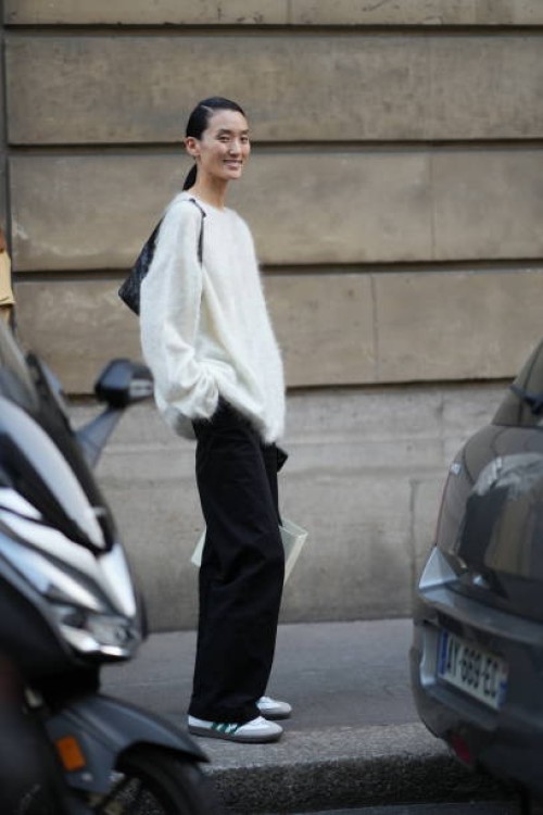 Model wears a white fluffy pullover, a bag, black flared pants, sneakers, outside Victoria Beckham, during the Womenswear Spring/Summer 2024 as part...