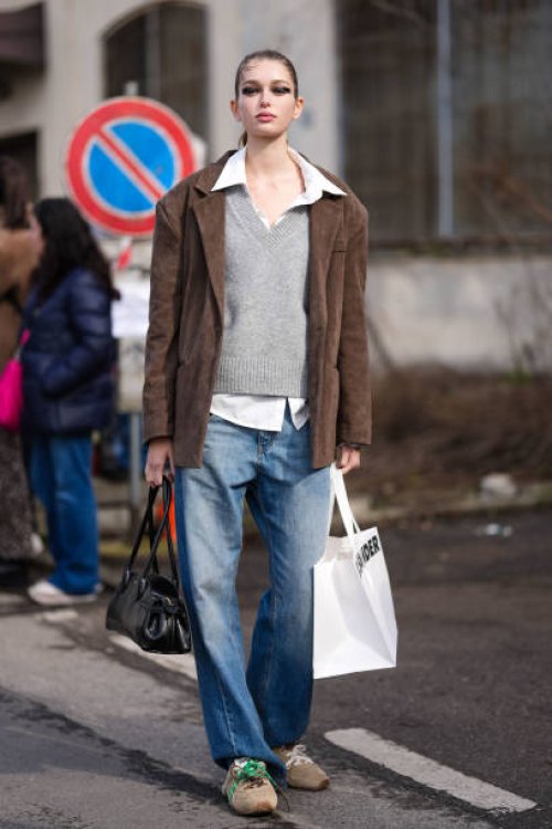 Model wears black straight eyeshadow, white oversized buttoned up long sleeve shirt, light gray v-neck oversized sweater, dark brown oversized suede...