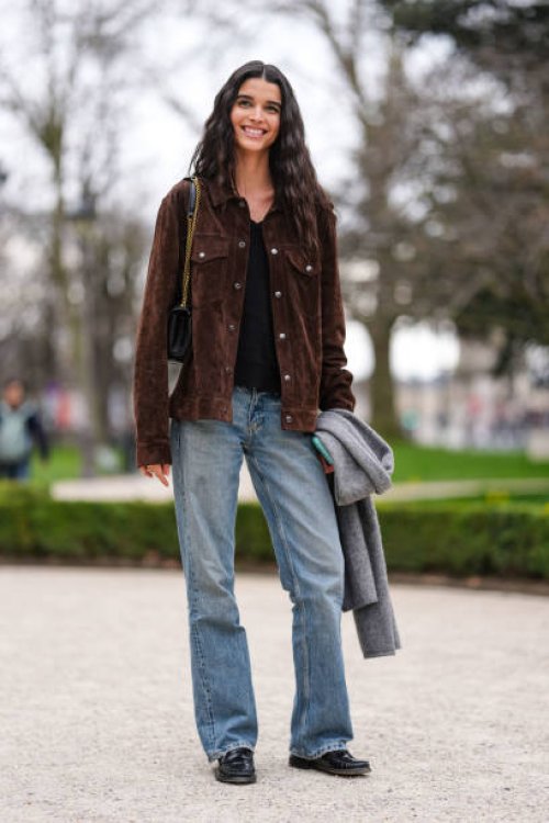 Model wears black t-shirt, dark brown suede jacket, shiny black leather bag, light blue denim jean pants, shiny black loafer moccasin leather shoes,...