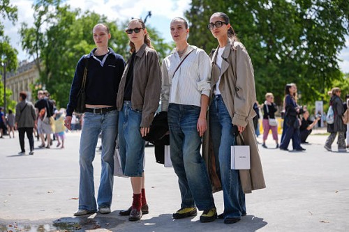 Model wears black t-shirt, navy blue long sleeve Miu Miu sweeter, shiny black leather bag, black leather belt, navy blue washed denim jean pants,...
