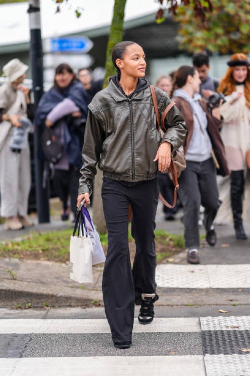 Model wears dark brown leather bomber jacket, black fitted pants, dark brown leather bag, outside Chloe, during the Paris Fashion Week Spring/Summer...
