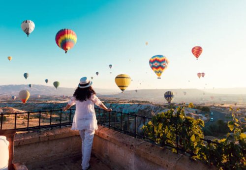 mooie aziatische vrouw kijken kleurrijke hete lucht ballonnen vliegen over de vallei in cappadocië, turkey.turkey cappadocië sprookjesachtige landschap van bergen. turkije cappadocië sprookjesachtige landschap van bergen. - t