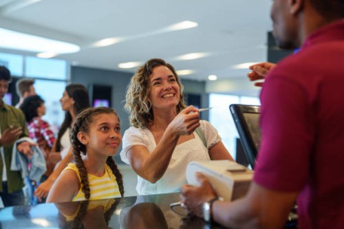mother and daughter cheerfully buying movie tickets at movie theater box office - junk food stock pictures, royalty-free photos & images