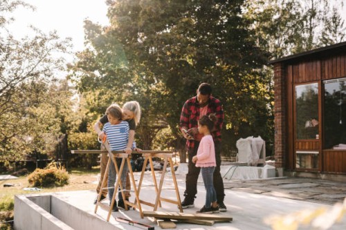mother and son using hand saw while father talking to daughter outside house - garden decoration photos et images de collection
