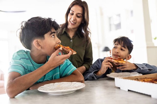 mother and young boys eating pizza in kitchen - junk food stock pictures, royalty-free photos & images