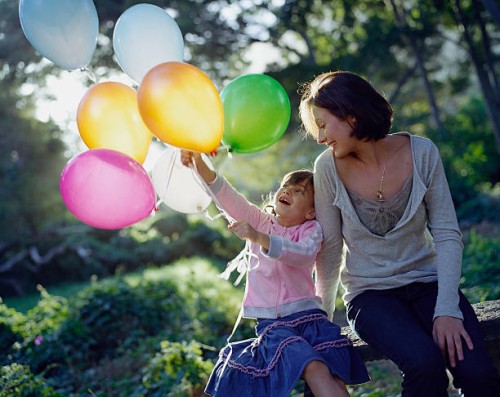 mother with daughter (6-7) holding balloons sitting in garden - garden decoration stock pictures, royalty-free photos & images