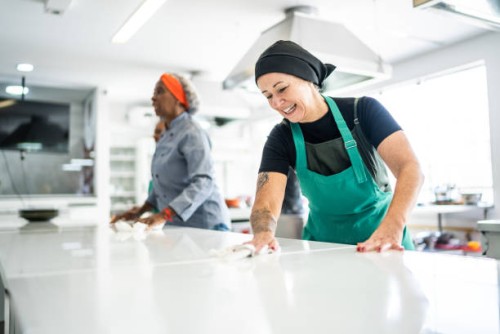 mujer madura limpiando el mostrador de la cocina en la cocina comercial - food fotografías e imágenes de stock
