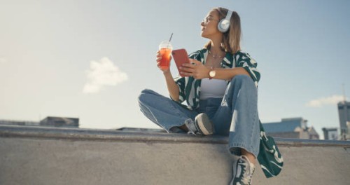 mujer, smartphone en la ciudad y bebida, escuchando música y mirando la vista del paisaje urbano, streaming y verano. joven mujer relájese en un parque urbano, lista de reproducción de audio y radio con té helado y gen z - fa