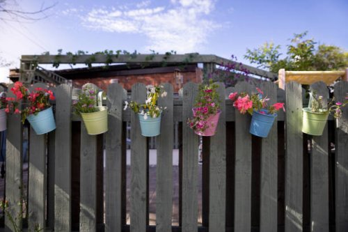 multi-coloured, decorative, metal plant pots containing flowering plants, hanging from a wooden fence in a back yard on a sunny day in summertime. - garden decoration stock pictures, royalty-free photos & images