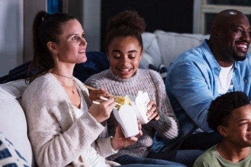 multi-ethnic family on couch watching tv, eating takeout - junk food stock pictures, royalty-free photos & images