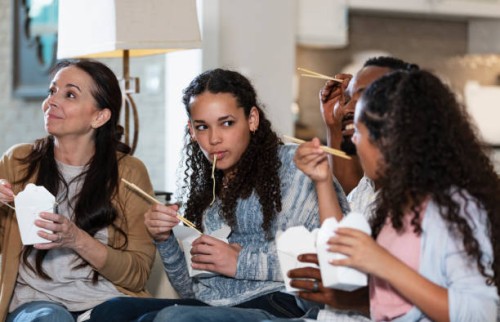 multiracial family watching tv, eating take out food - junk food stock pictures, royalty-free photos & images